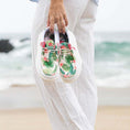 Load image into Gallery viewer, A woman walking on the beach with the ocean in the background with a pair of Gator Waders Camp Shoes in her hand.