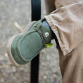 Load image into Gallery viewer, A guy crossing his legs and wearing a pair of Camp Shoes. The color of the shoes is olive.