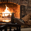 Load image into Gallery viewer, A guy propping his feet up by a fireplace while wearing a pair of olive Camp Shoes.