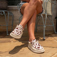 Load image into Gallery viewer, A woman sitting in a chair with her legs crossed. She is wearing Camp Shoes in a brown cow pattern on her feet.