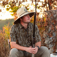 Load image into Gallery viewer, man sitting in chair wearing a straw hat in mossy oak original bottomland