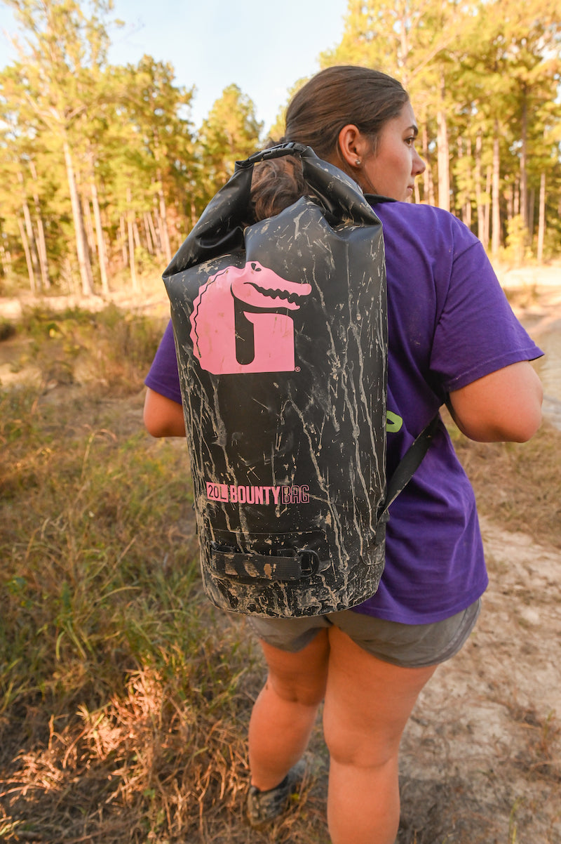 Girl walking through the woods with a 20L Bounty Bag from Gator Waders on her back.