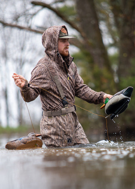 Man in camouflage waders holding a duck in a flooded forest
